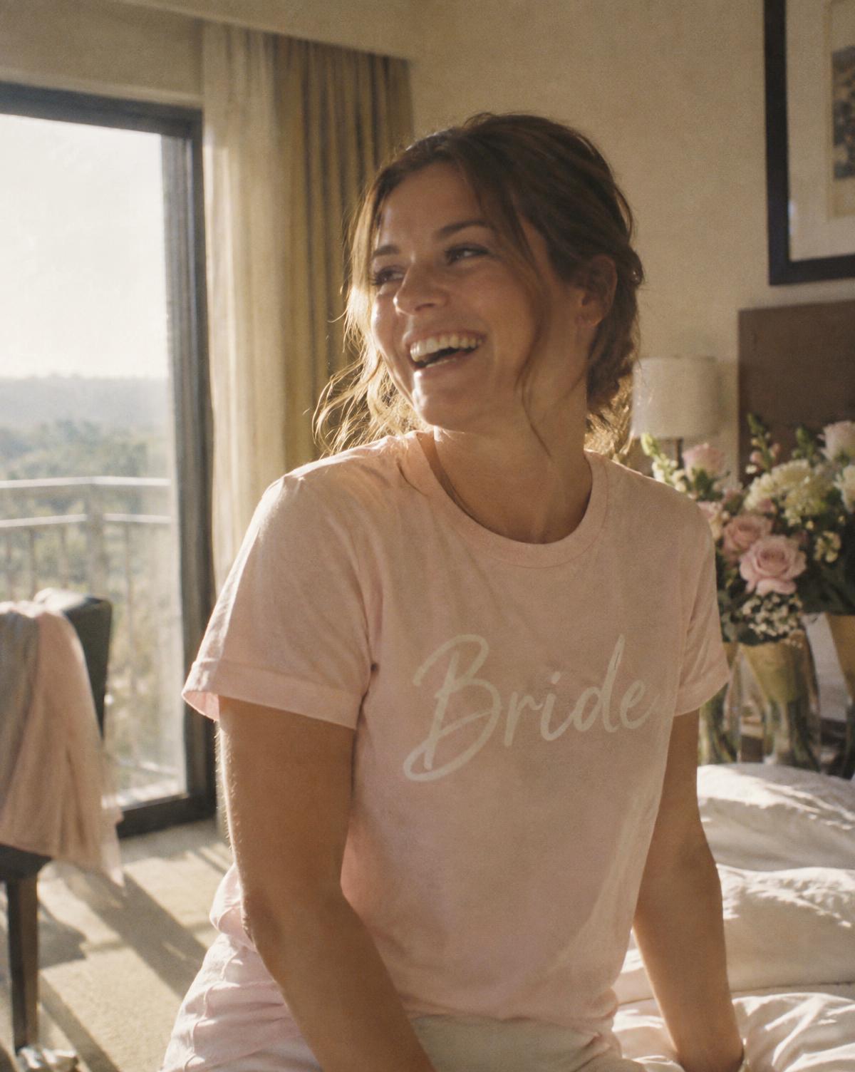 Laughing bride in a pale pink tee with white Bride script