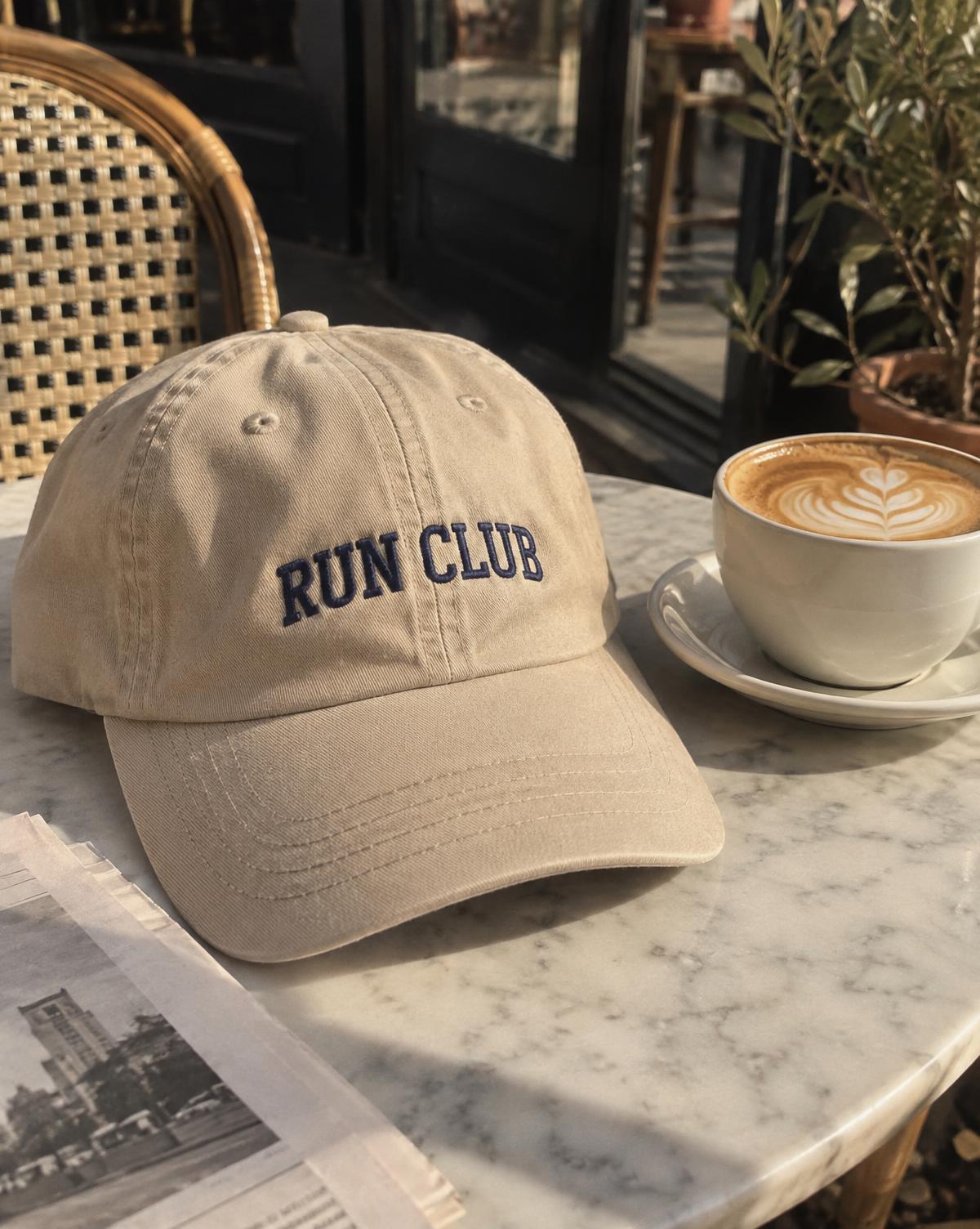 Sand dad cap with navy embroidered Run Club lettering next to a flat white